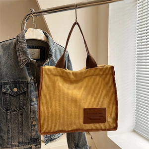 Yellow corduroy tote bag with brown straps and fashion label hanging in soft light