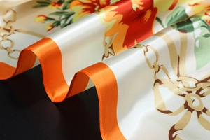 Close-up of cream satin scarf with vibrant orange floral prints and gold chain patterns