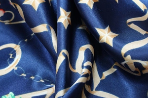 Detail of navy blue satin scarf featuring beige star and chain patterns with silk luster