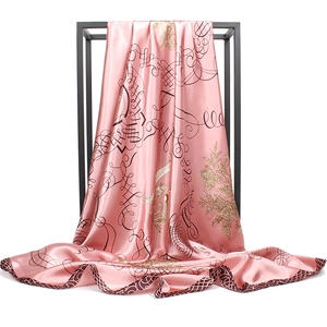 Pink satin square silk scarf with golden floral patterns on a minimal black display stand