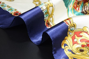 Macro view of satin silk scarf featuring golden chain patterns and vintage crest details