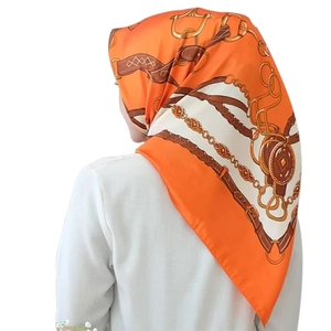 Detailed view of horse-bit and gold chain print on orange satin square scarf worn by model