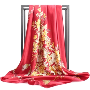 Detailed view of red silk scarf with yellow floral prints hanging on a black stand