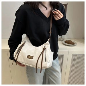 Détail du sac bandoulière demi-lune crème avec zips à pompons bruns porté par un mannequin