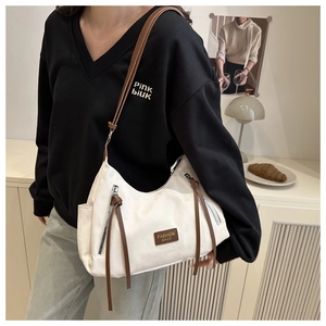 Détail du sac à bandoulière en toile blanche avec finitions en cuir marron sur modèle