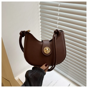 Détail d'un sac demi-lune marron avec fermoir tournant doré et bandoulière à nœuds élégante