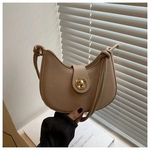 Détail du sac demi-lune beige avec fermoir doré tournant et bandoulière à nœud décoratif