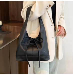 Detail of a black pleated tote bag with bow accent on a model in beige blazer
