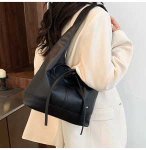Detail of black wax leather tote bag with bow drawstring on a model in beige suit