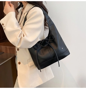 Detail of black matte leather tote bag featuring a bow tie and silver heart emblem