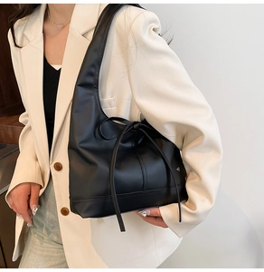 Detail of a black leather tote bag with a decorative bow knot worn by a model in a suit