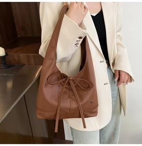 Detail of a brown leather tote bag with a bow knot and heart metal charm on a model