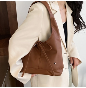 Brown leather tote bag featuring a bow tie design and heart metal accent worn by a model