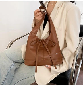 Detail of a brown pleated tote bag featuring a decorative bow and heart pendant