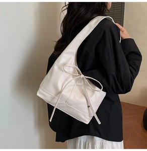 Detail view of white leather tote with bow knot accessory worn by model