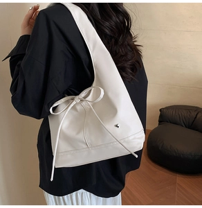 Detail of white PU leather shoulder bag with decorative ribbon bow and heart metal charm