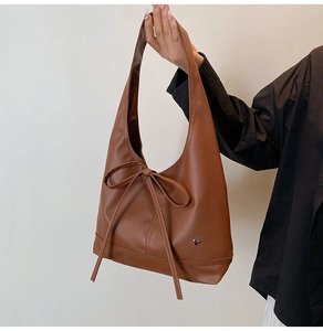 Détail d'un sac hobo en cuir huilé marron foncé avec un nœud et un pendentif cœur argenté