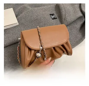 Detail of ruched brown leather shoulder bag with golden chain and metal sphere charm