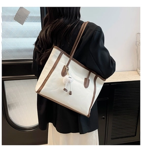 Detail of a large cream tote bag with dark brown trim worn on a shoulder with a plush charm