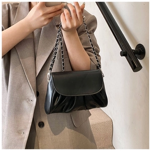 Detail van zwarte geplooide handtas met kettingriem gedragen op een bruine blazer