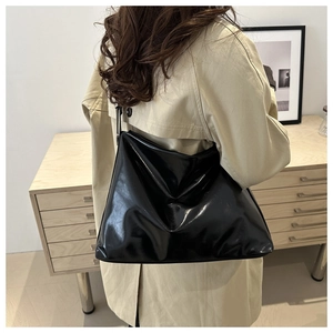 Sac fourre-tout noir brillant avec large bandoulière porté par un mannequin en trench