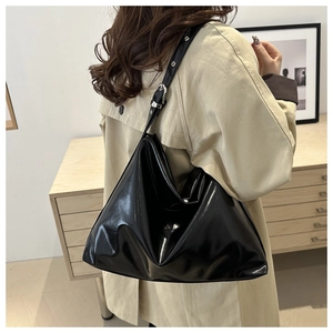 Side view of black glossy patent leather tote bag with silver hardware on a model