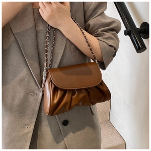 Detail of a brown ruched cloud bag featuring glossy leather and a silver metal chain strap