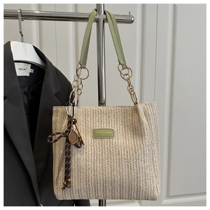 Detail of straw woven tote bag featuring light green leather chain strap and tennis charm