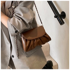 Detail van de donkerbruine geplooide crossbodytas met ketting op een grijze blazer