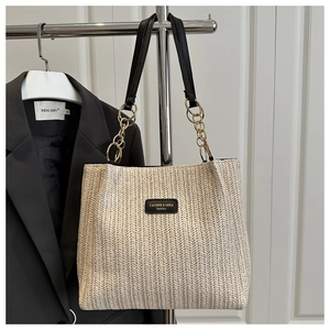 Detail of woven straw bucket bag with black leather logo patch and gold chain strap