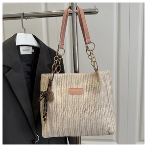 Detail of woven straw tote bag with pink leather handle and gold chain hardware accents