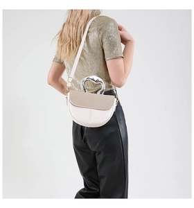 Detail of a chic cream saddle bag with metallic handle shown on model in studio