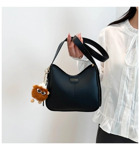 Détail du sac croissant en cuir noir avec logo doré et pendentif monstre en peluche doux