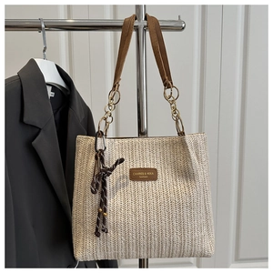 Detail of woven straw tote bag featuring brown leather strap and golden chain link