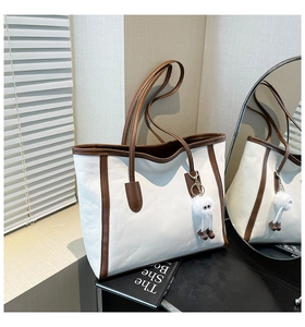 Detail of canvas tote bag with brown leather trim and cute plush monster pendant charm