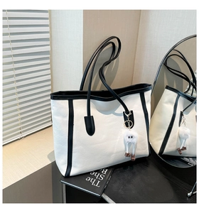 Detail of white tote bag with black trim and a cute plush toy pendant on the side