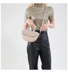 Detail of beige saddle bag featuring woven texture flap and metallic silver circular handle
