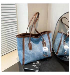 Detail of denim tote bag with leather trim and a cute plush doll charm accessory