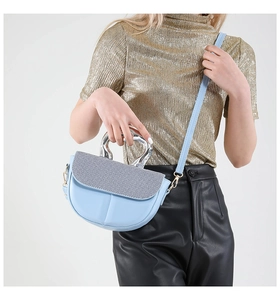 Close-up of light blue leather saddle bag featuring silver glitter flap and U-shaped handle