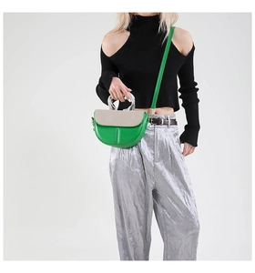 Detail of a green and beige patchwork saddle bag with a silver metal handle on model