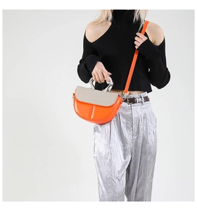 Detail of orange saddle bag with woven texture flap and transparent curved top handle