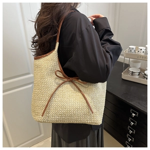 Detailed side view of woven straw tote bag with brown leather bow on a model