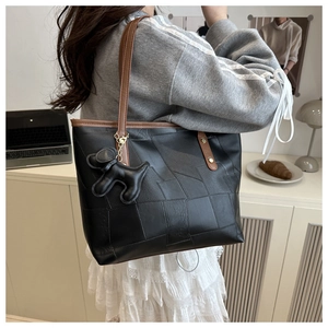 Détail du sac cabas avec coutures géométriques, lanières brunes et breloque chien