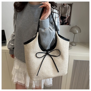 Detail of beige woven straw tote bag with black leather handles and decorative bow