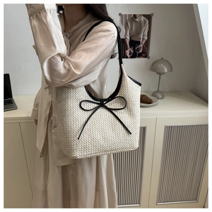 Detail of knit tote bag with black leather bow and slender strap on a neutral background