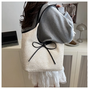 Close-up of woven straw tote bag with black leather trim and bow knot detail