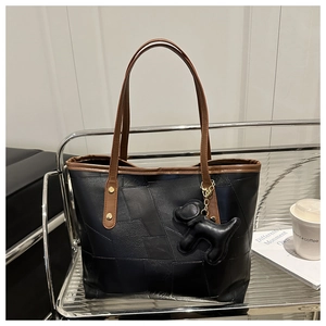 Detail of black patchwork tote bag with brown straps and cute dog charm on a display