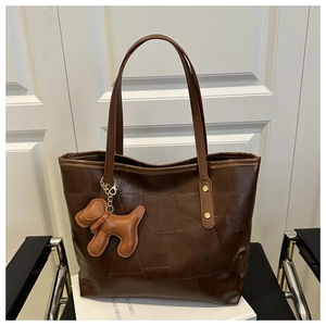 Detail of dark brown patchwork leather tote bag with dog charm and gold stud accents