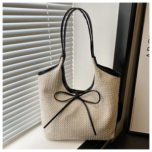 Detail of hand-woven straw tote bag with black faux leather trim and bow knot