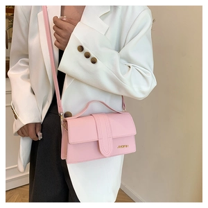 Détail du mini sac carré rose clair avec logo JINGPIN doré et poignée sur blazer blanc